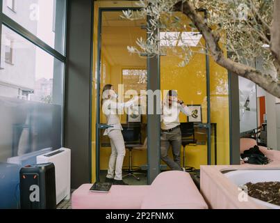 Deux collègues masculins et féminins attrayants ayant un appel téléphonique dans les cabines téléphoniques au bureau Banque D'Images