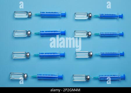 Seringues jetables avec aiguilles et flacons sur fond bleu clair, à plat Banque D'Images