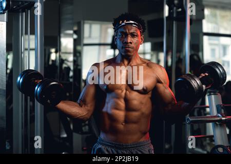 20s Noir et musclé dans une salle de gym montrant des haltères et ses muscles. Banque D'Images