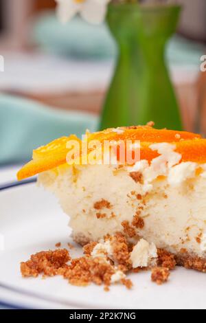 Une photo en gros plan d'une tranche de gâteau au fromage aux agrumes surmontée de tranches d'orange confites sur une assiette blanche avec un fond doux. Banque D'Images