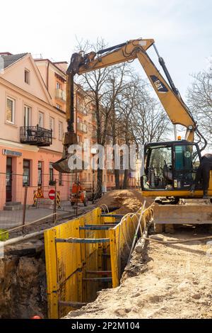 Grodno, Bélarus - 06 mars 2022: Pelle hydraulique remplissant une excavation profonde soutenue par une boîte de tranchée avec des tuyaux de litière de gravier de pois pendant l'installation de draina Banque D'Images