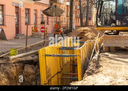 Grodno, Bélarus - 06 mars 2022: Pelle hydraulique remplissant une excavation profonde soutenue par une boîte de tranchée avec des tuyaux de litière de gravier de pois pendant l'installation de draina Banque D'Images