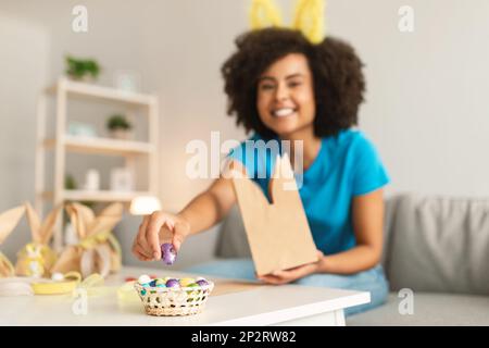 Gâteries de Pâques. Femme noire qui fait l'emballage des œufs de chocolat dans un sac en papier à la maison Banque D'Images