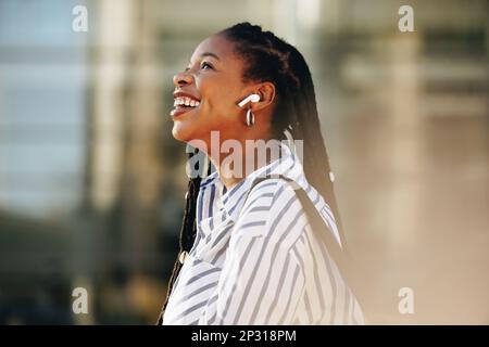 SideView d'une jeune femme d'affaires joyeuse écoutant de la musique sur son chemin pour travailler dans la ville. Bonne femme d'affaires appréciant une liste de lecture du matin sur elle Banque D'Images