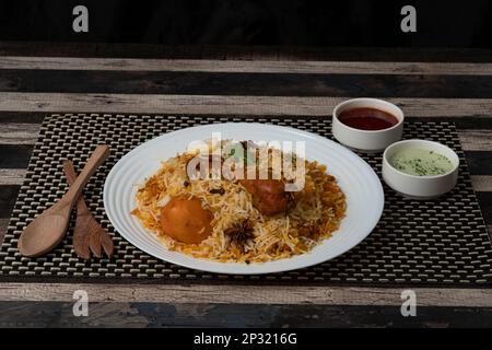 Poulet Biryani, cuisine indienne pakistanaise populaire dans une assiette blanche sur fond texturé foncé. Banque D'Images