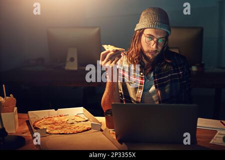 Concepteur Web, homme avec pizza à l'ordinateur portable et quart de nuit, heures supplémentaires et échéance à l'agence de marketing numérique. Recherche de contenu, lecture et homme sérieux Banque D'Images