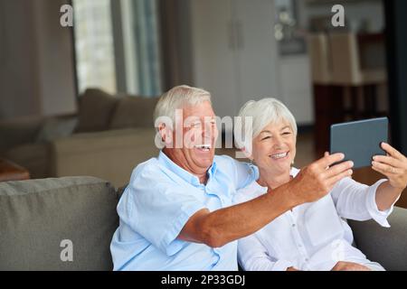 Voyons comment un couple doit faire un selfie. un couple senior prend un selfie avec sa tablette à la maison. Banque D'Images