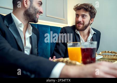 Deux jeunes hommes sont assis dans un restaurant, prenant le petit déjeuner et la conversation. Ils sont tous deux vêtus de vestes et de chemises, et ont des verres de fruits Banque D'Images