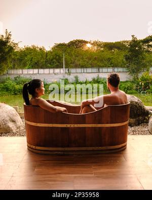 Couple hommes et femmes dans une baignoire en bois à la campagne de la Thaïlande regardant le coucher du soleil. Banque D'Images