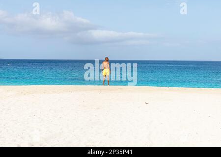 Local hommes en maillot de bain jaune debout sur une belle plage de sable blanc Laginha dans le centre-ville de Mindelo ville sur l'île de Sao Vicente, Cabo verde Banque D'Images