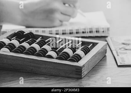 Vieux bois abacus pour compter de l'argent sur une table en bois et une main de femme écrit dans un carnet, et l'argent se trouve à proximité noir et blanc photo de gros plan Banque D'Images