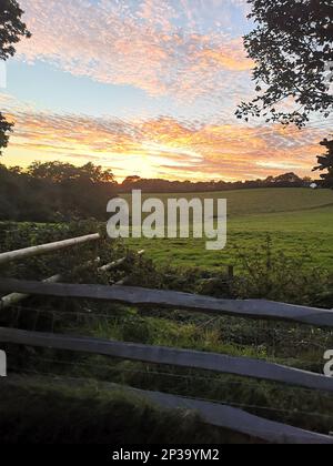 Vue sur un coucher de soleil sur une prairie avec une clôture en bois au premier plan. Banque D'Images