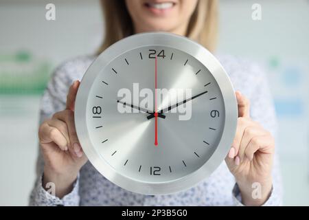 Elle tient une horloge ronde près de son corps. Banque D'Images