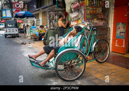 Un conducteur de cyclo traditionnel a un sommeil dans son pédicab en bas d'une route latérale à Phnom Penh, Cambodge. Banque D'Images