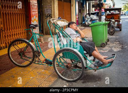 Un conducteur de cyclo traditionnel a un sommeil dans son pédicab en bas d'une route latérale à Phnom Penh, Cambodge. Banque D'Images