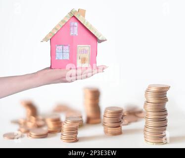 augmentation des loyers, taux d'intérêt, frais de chauffage, frais de vie, modèle de maison à la main des femmes avec l'argent empilé en arrière-plan, conceptuel, pictur symbolique Banque D'Images