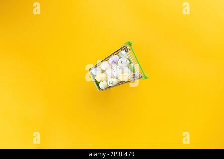 Différents œufs de caille, blancs et colorés, se trouvent dans un panier sur fond jaune. Vue de dessus, espace vide Banque D'Images