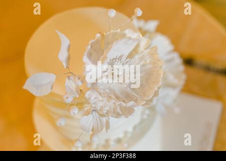 Un élégant gâteau de mariage blanc avec des décorations florales délicates est placé sur une table jaune vif, suggérant les joies d'une occasion spéciale Banque D'Images