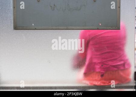 Dame dans un manteau rose assis dans un abri de bus avec des murs en verre dépoli. Bruxelles. Banque D'Images