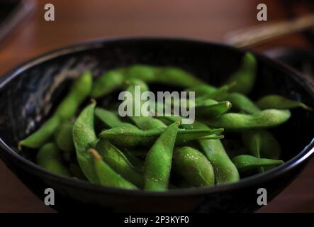 Un bol noir rempli d'edamame salé. Banque D'Images