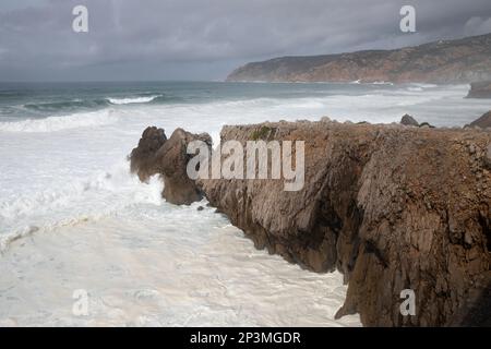 Vagues de l'océan Atlantique orageux s'écrasant sur des rochers sous forte do Guincho en regardant vers le nord jusqu'à la pointe de Ponta do Rebolo Banque D'Images