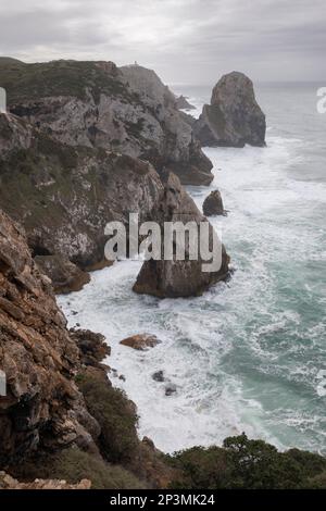 Vagues de l'océan Atlantique se déroulant sur les rochers de Pedra de Alvidrar avec vue vers le sud sur le phare de Cabo da Roca Banque D'Images