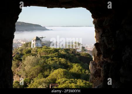 Le moulin à vent en ruines de Moinho do Facho se trouve à la campagne dans la brume matinale vue à travers le trou dans les murs de la ville d'Obidos, Obidos, région centrale, Portugal, Europe Banque D'Images