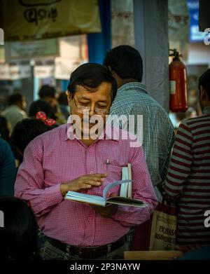 Kolkata, Inde - 12 février 2023 : un homme s'est engrosé dans la lecture d'un livre au milieu de la foule vibrante de la foire du livre de Kolkata. Mise au point sélective. Banque D'Images