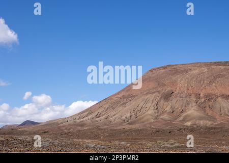 Impressionnant Red Mountail (Montana Roja), entouré par le désert. Ciel bleu vif en hiver avec quelques nuages blancs. Corralejo, Fuerteventura, Canary I Banque D'Images