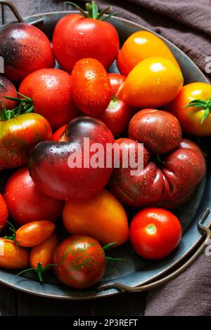 Tomates de différentes variétés et tailles sur un plateau en fer sur une table en bois. Banque D'Images