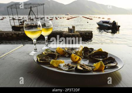 Monténégro. Ferme ostréicole. Coucher de soleil. Sur la table se trouve une assiette d'huîtres et de citron et deux verres de vin blanc Banque D'Images