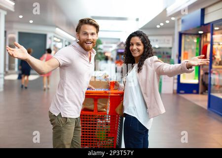 un jeune couple heureux dans le hall du supermarché avec chariot Banque D'Images