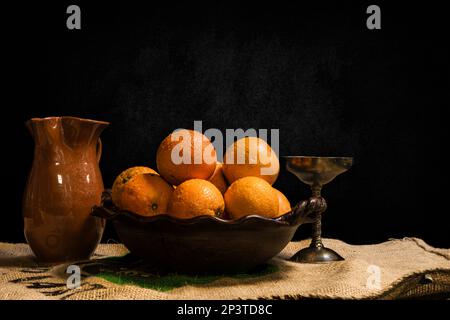 encore la vie de fruits bananes oranges citrons pommes sur une casserole d'argile sur un fond sombre Banque D'Images