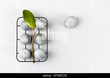 Œufs de Pâques gris avec une branche et une feuille de magnolia sur fond gris. Minimalisme, espace de copie, pose à plat Banque D'Images