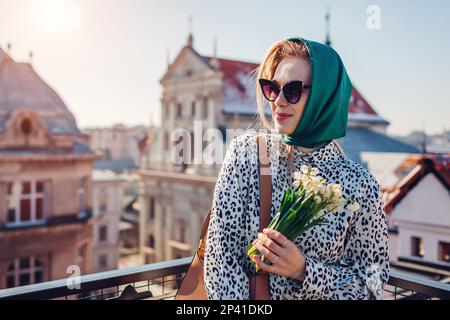 Jeune femme élégante portant un châle rétro vert avec des lunettes de soleil tenant des fleurs de printemps. Style vintage classique en extérieur Banque D'Images