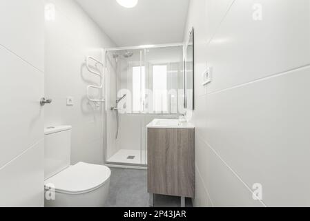 Petite salle de bains avec un lavabo carré en porcelaine blanche sur une armoire en bois, un miroir sans cadre sur le mur et une cabine de douche à parois de verre Banque D'Images