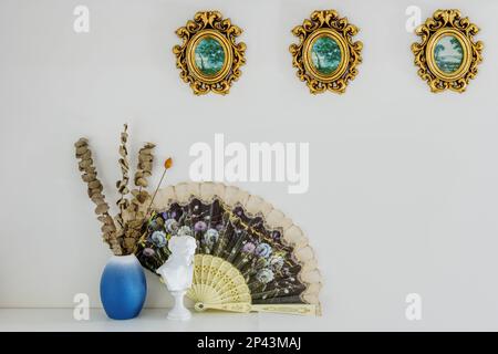 Étagère en bois avec objets décoratifs avec cadres en bois doré, vases avec plantes séchées et un ventilateur à motifs Banque D'Images