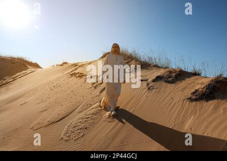 Homme en vêtements arabes marchant dans le désert le jour ensoleillé Banque D'Images