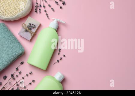 Composition de pose plate avec bouteilles de gel douche et fleurs de lavande sur fond rose, espace pour le texte Banque D'Images