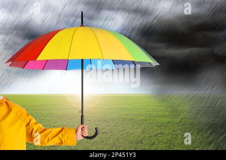 Femme avec parapluie ouvert lumineux sous une forte pluie dans le champ vert, gros plan Banque D'Images