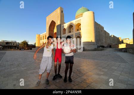 Des garçons ouzbèkes jouant au football par la mosquée de Kalan dans la vieille ville de Boukhara, Ouzbékistan. Banque D'Images