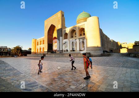 Des garçons ouzbèkes jouant au football par la mosquée de Kalan dans la vieille ville de Boukhara, Ouzbékistan. Banque D'Images