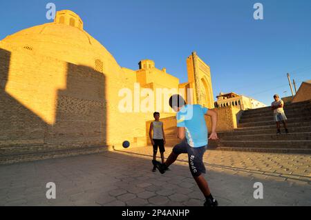 Des garçons ouzbèkes jouant au football par la mosquée de Kalan dans la vieille ville de Boukhara, Ouzbékistan. Banque D'Images