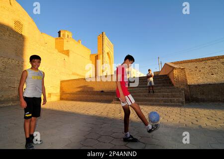 Des garçons ouzbèkes jouant au football par la mosquée de Kalan dans la vieille ville de Boukhara, Ouzbékistan. Banque D'Images