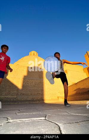 Des garçons ouzbèkes jouant au football par la mosquée de Kalan dans la vieille ville de Boukhara, Ouzbékistan. Banque D'Images