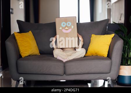 Portrait de style de vie d'un enfant jouant avec une boîte en carton sur le canapé dans la salle de séjour. Mignon enfant portant un costume robot à la maison Banque D'Images