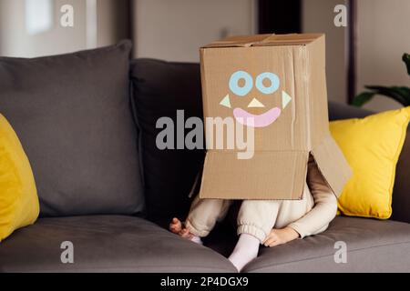 Portrait de style de vie d'un enfant jouant avec une boîte en carton sur le canapé dans la salle de séjour. Mignon enfant portant un costume robot à la maison Banque D'Images