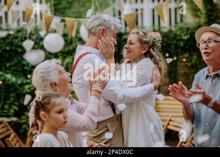 Mariée et marié matures célébrant le mariage avec leur famille, à l'extérieur de l'arrière-cour. Banque D'Images