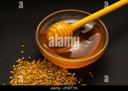 Une cuillère jaune de miel trempée dans un pot de miel et de pain d'abeille éparpillés sur fond noir. Le miel coule autour, belles et invitantes photos Banque D'Images