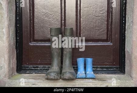 Deux paires de bottes en caoutchouc, une paire de bottes pour enfants et une paire de bottes pour hommes, à l'extérieur de la porte de la ferme, Whitewell, Lancashire, Angleterre, United Banque D'Images